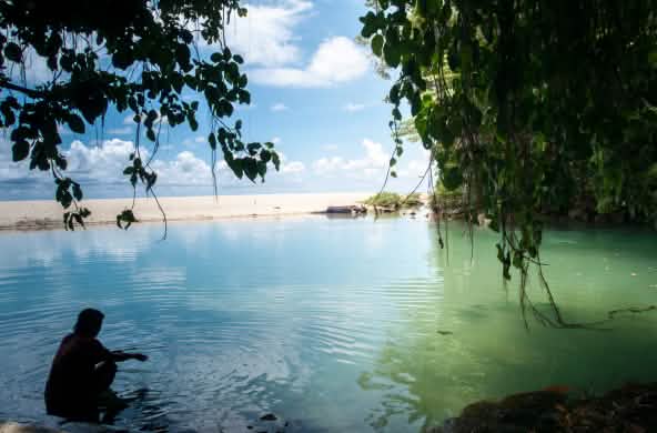 Una donna in una baia circondata da acqua, rocce e sabbia