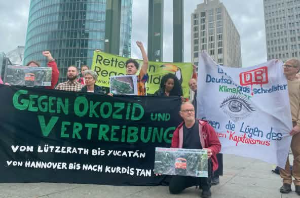 Un gruppo di persone protesta con grandi striscioni colorati davanti a tre edifici per uffici