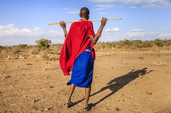 Persona Masai di spalle, con in mano un bastone di legno.