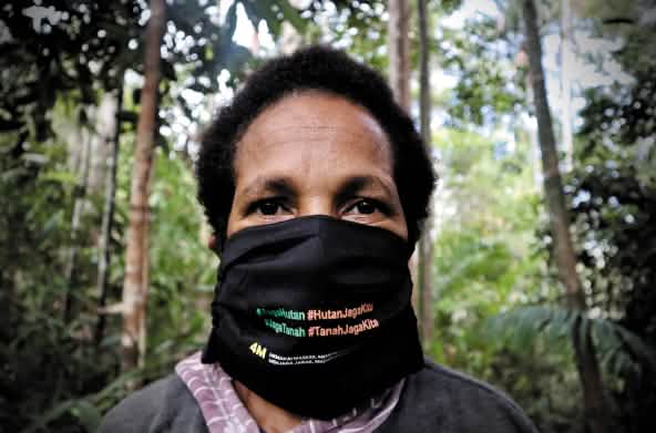 Donna papuana che indossa una maschera con la scritta "Proteggi la foresta - la foresta ci protegge".