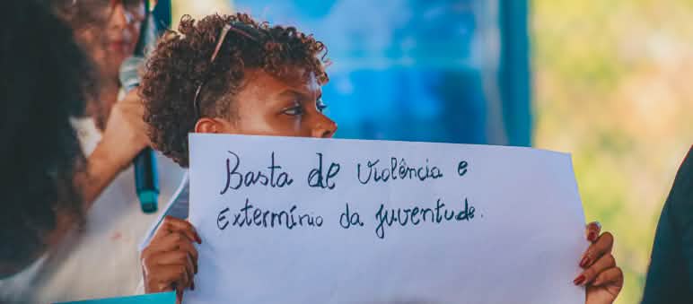 I giovani che hanno partecipato al congresso sono ex partecipanti al laboratorio di comunicazione popolare organizzato dalla CPT Maranhão in collaborazione con Salviamo la Foresta Una giovane donna tiene un cartello con la scritta “Basta con la violenza e lo sterminio dei giovani”